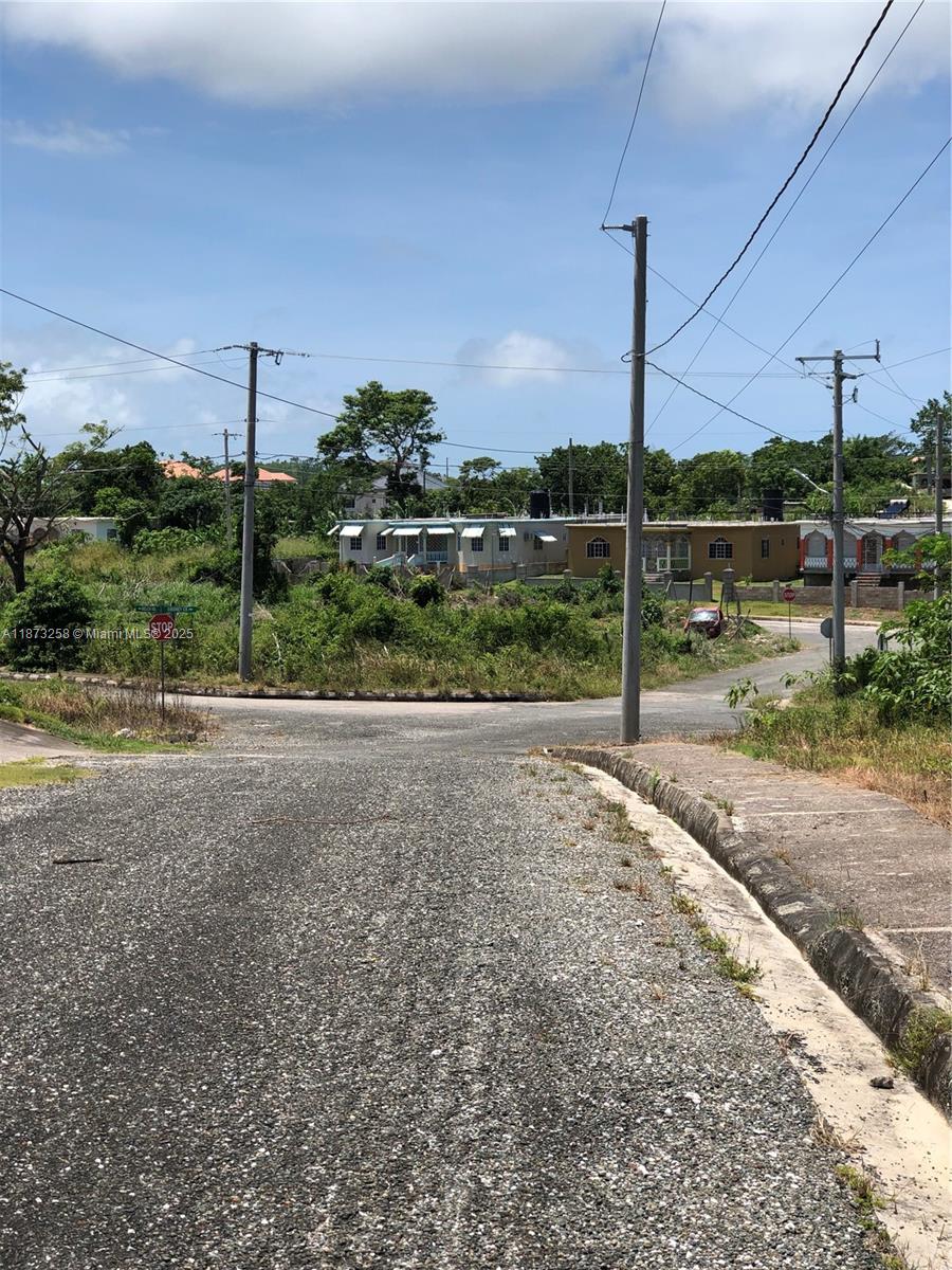 An asphalt road leads to an intersection with utility poles and residential buildings in the background — MINARD PEN PART OF MAINARD PEN, JA, JA