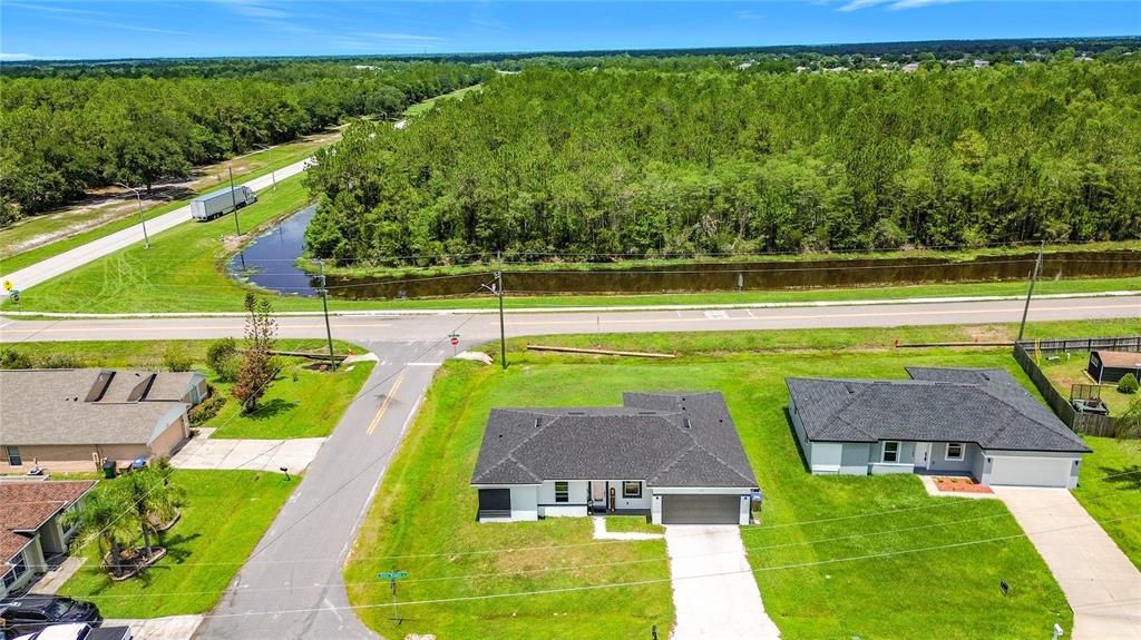 An aerial view shows two suburban houses near a road, a canal, and dense woods — 1101 SAINT TROPEZ COURT, KISSIMMEE, FL