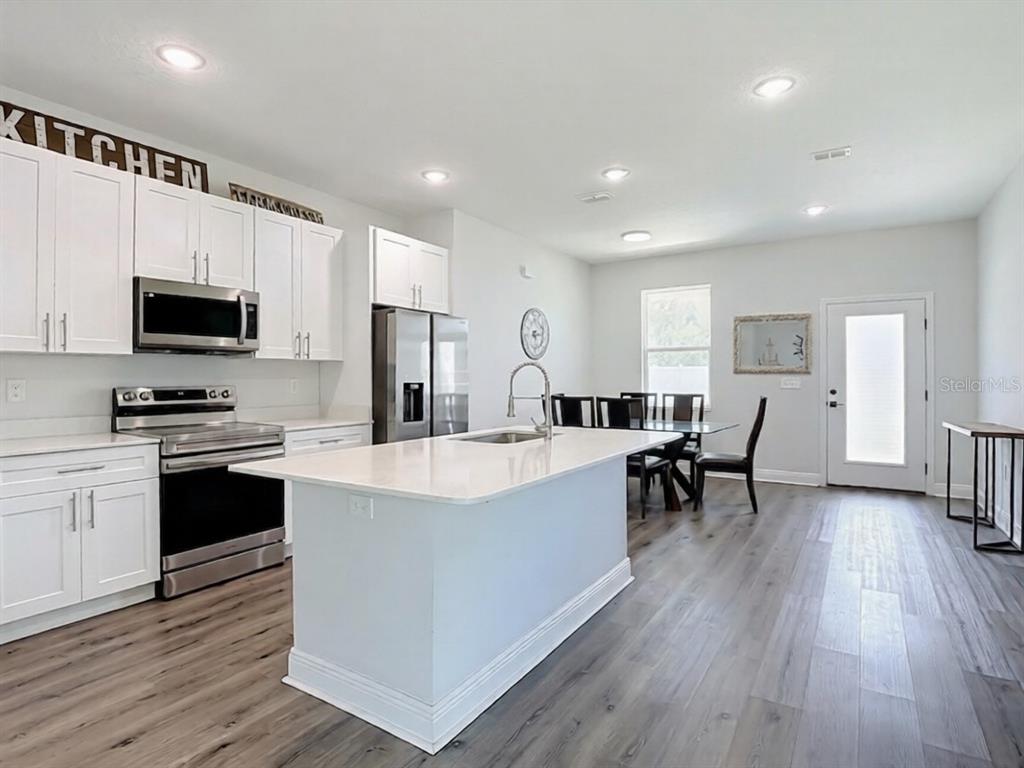 A modern kitchen features white cabinets, stainless steel appliances, a center island, and wood flooring — 1101 SAINT TROPEZ COURT, KISSIMMEE, FL