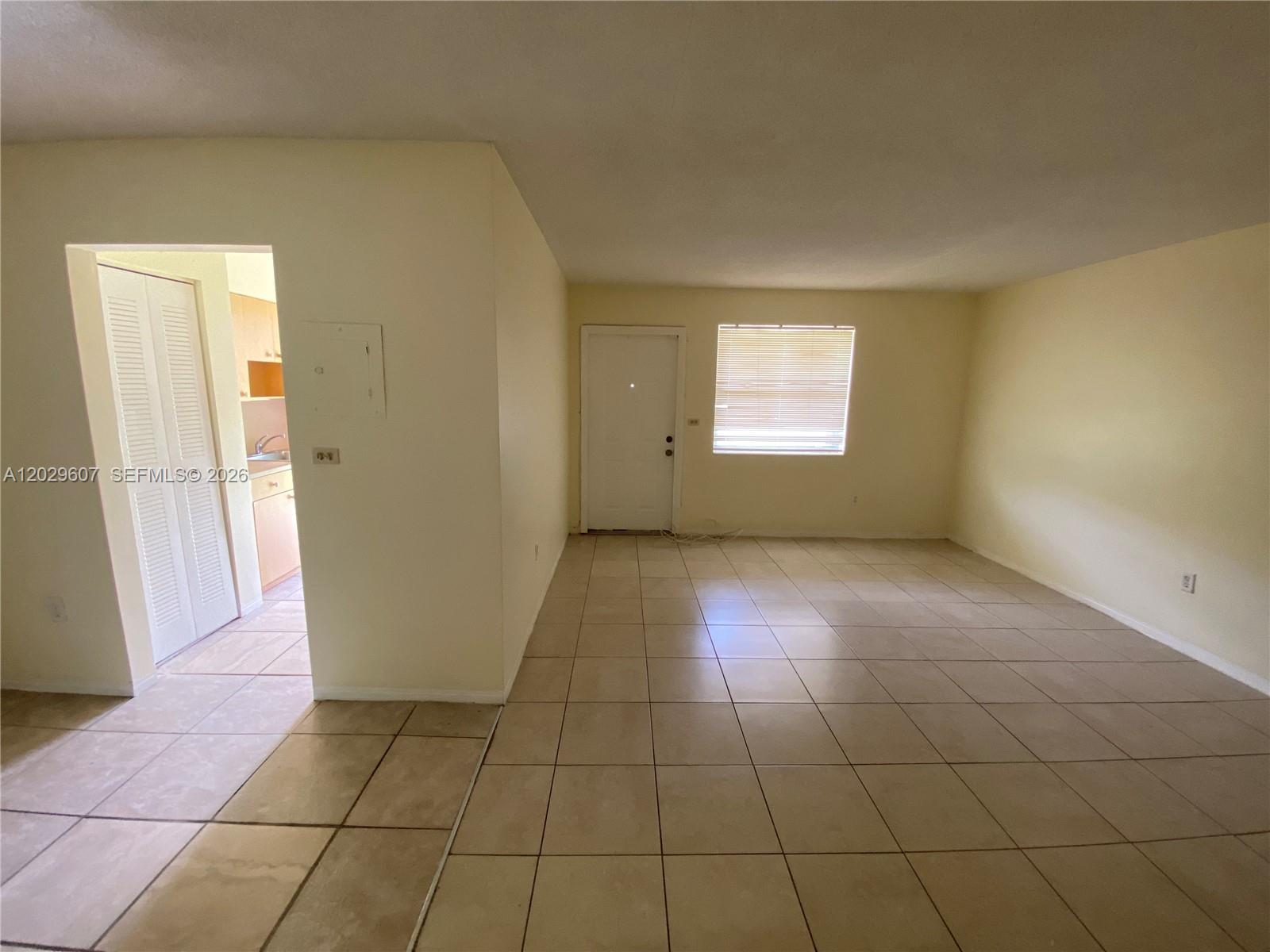 An empty room with beige tile flooring, a white door, and a window with blinds — 2400 NE 188th St # 2404, Miami FL 33180, MIAMI, FL
