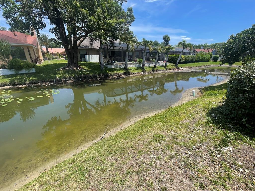 A view of a backyard canal with a house and palm trees in the background — 4696 LONG LAKE DRIVE, SARASOTA, FL