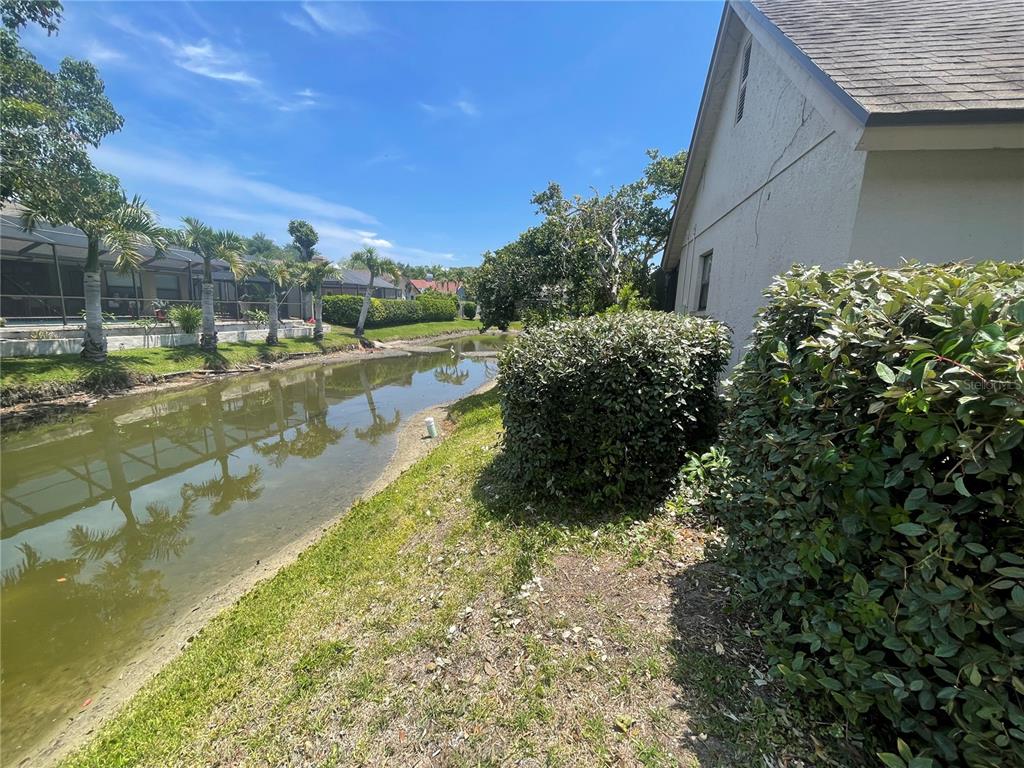 A view of a narrow canal behind a house with a large bush and palm trees — 4696 LONG LAKE DRIVE, SARASOTA, FL
