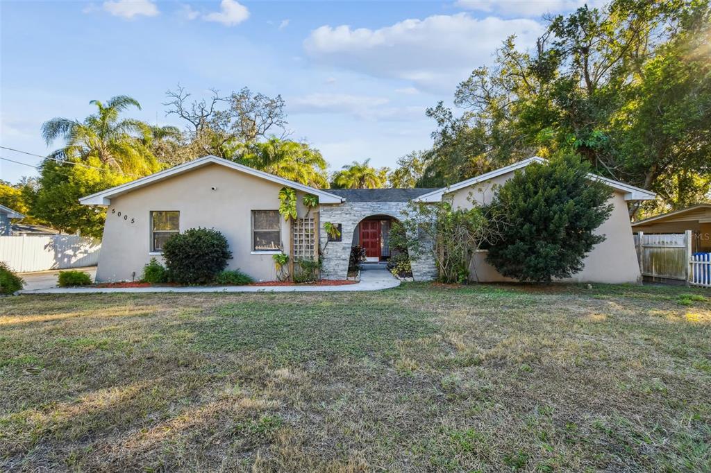 A single-story house with a beige stucco exterior, stone entryway, and a large front yard — 5005 PURITAN ROAD, TAMPA, FL