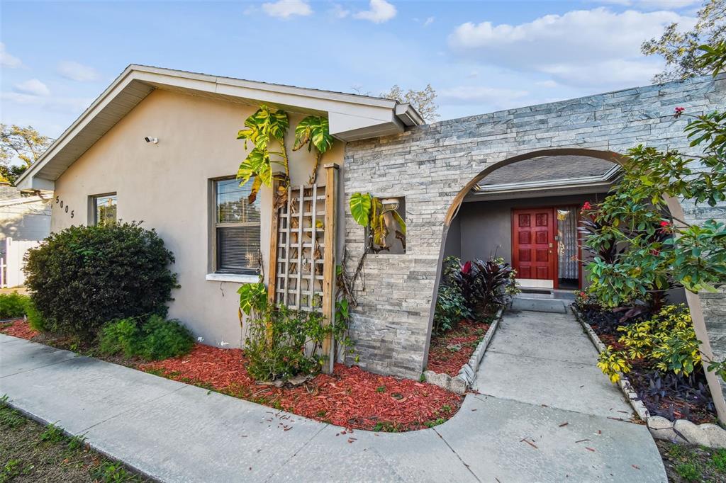 A house exterior features a stone-faced arched entryway, a red front door, and landscaping — 5005 PURITAN ROAD, TAMPA, FL