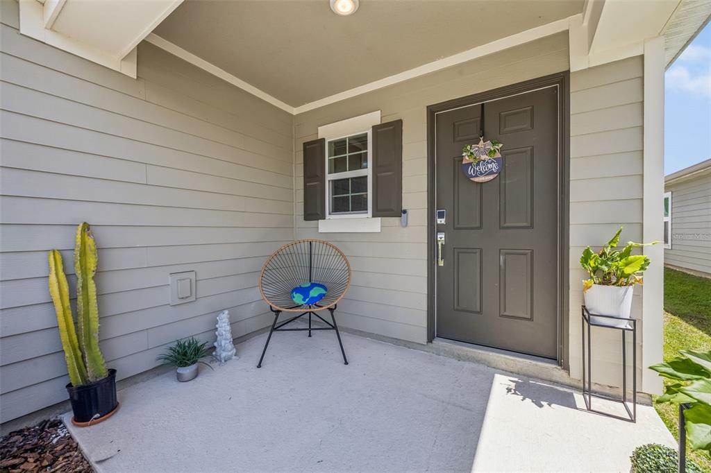 A covered front porch features a dark door, a round chair, and potted plants — 4366 SUNNY CREEK PLACE, KISSIMMEE, FL
