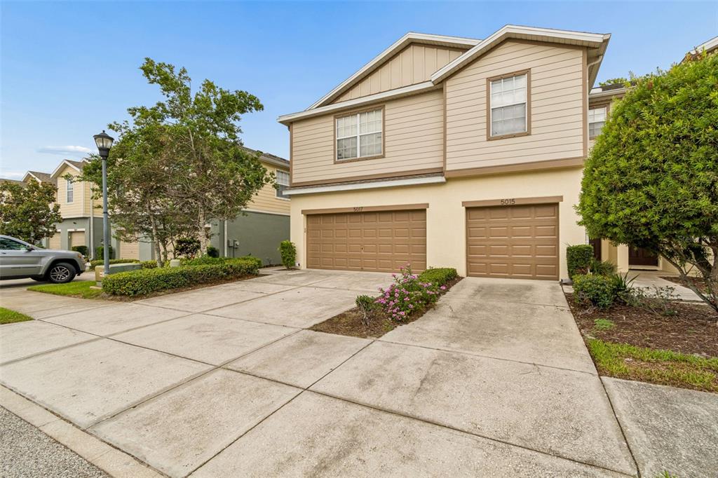 A two-story townhouse with tan siding, two brown garage doors, and a concrete driveway — 5017 WHITE SANDERLING COURT, TAMPA, FL