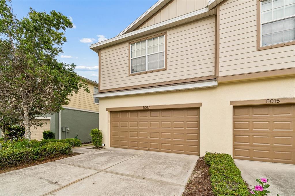A two-story townhouse exterior features tan siding, a beige stucco base, and two garage doors — 5017 WHITE SANDERLING COURT, TAMPA, FL
