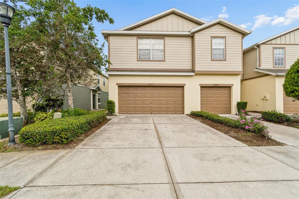 A two-story duplex with tan siding, two brown garage doors, and a concrete driveway — 5017 WHITE SANDERLING COURT, TAMPA, FL