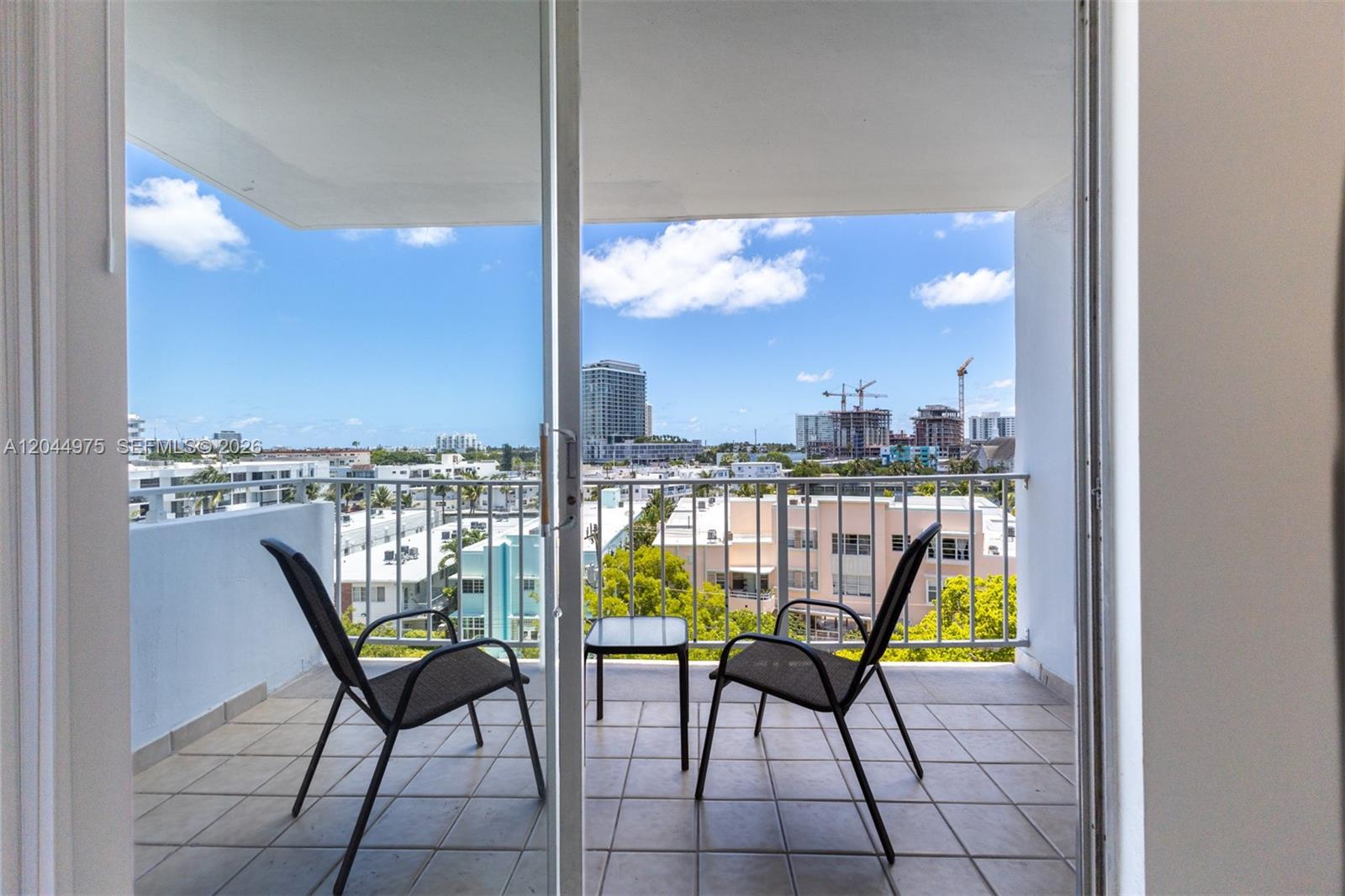 A balcony with two chairs and a small table overlooks a city skyline — 6900 Bay Dr # 6H, Miami Beach FL 33141, MIAMI BEACH, FL