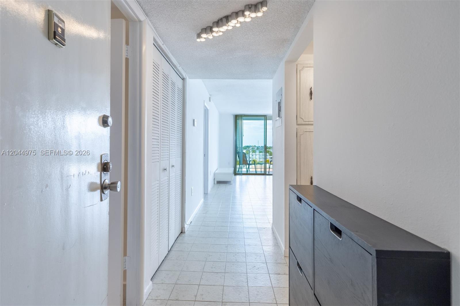 A hallway with white tile floors leads to a living area with a balcony view — 6900 Bay Dr # 6H, Miami Beach FL 33141, MIAMI BEACH, FL