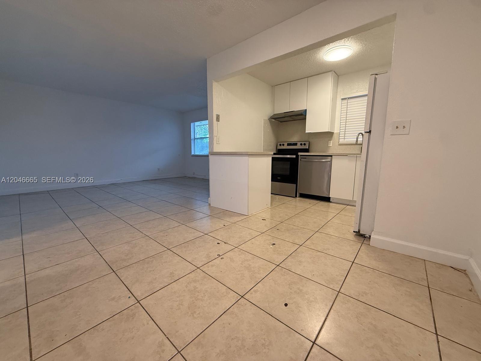 A kitchen with white cabinets and stainless steel appliances opens into a tiled living area — 400 NW 65th Ave # 202, Margate FL 33063, MARGATE, FL