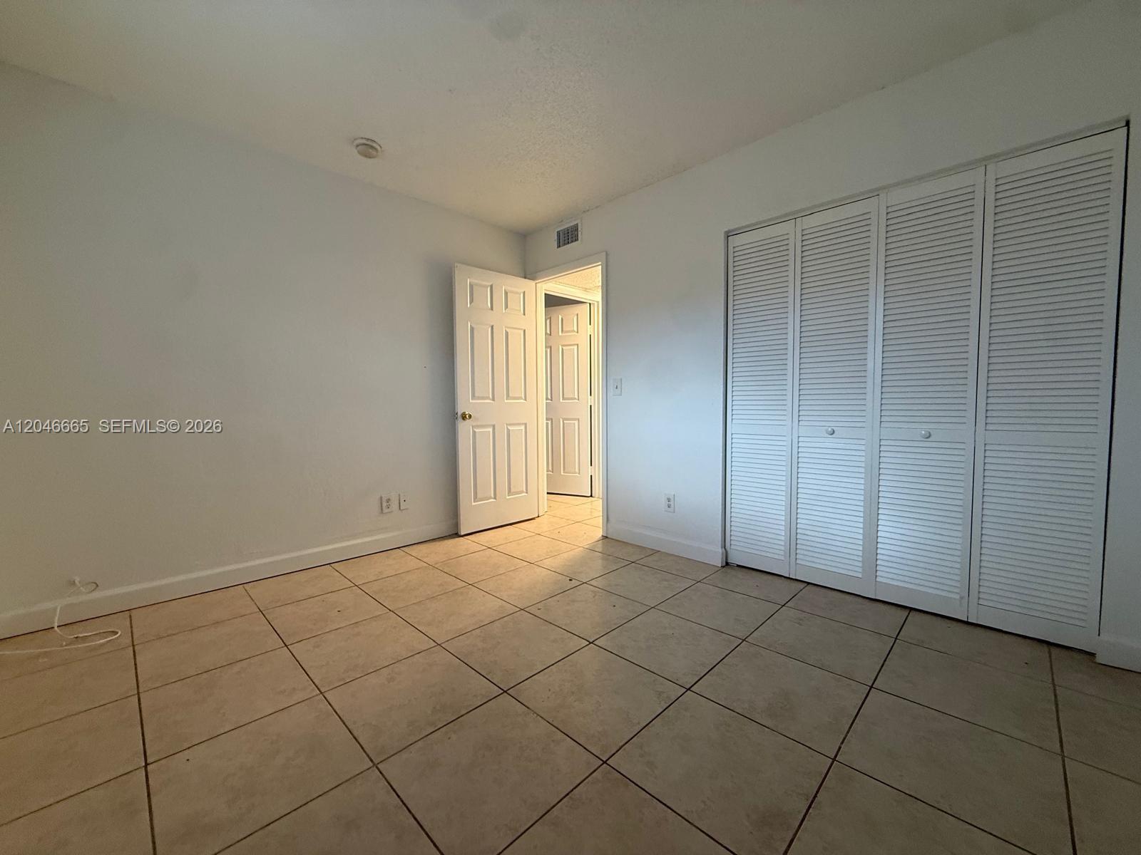 A room with white walls, tiled flooring, a closet with louvered doors, and an open doorway — 400 NW 65th Ave # 202, Margate FL 33063, MARGATE, FL