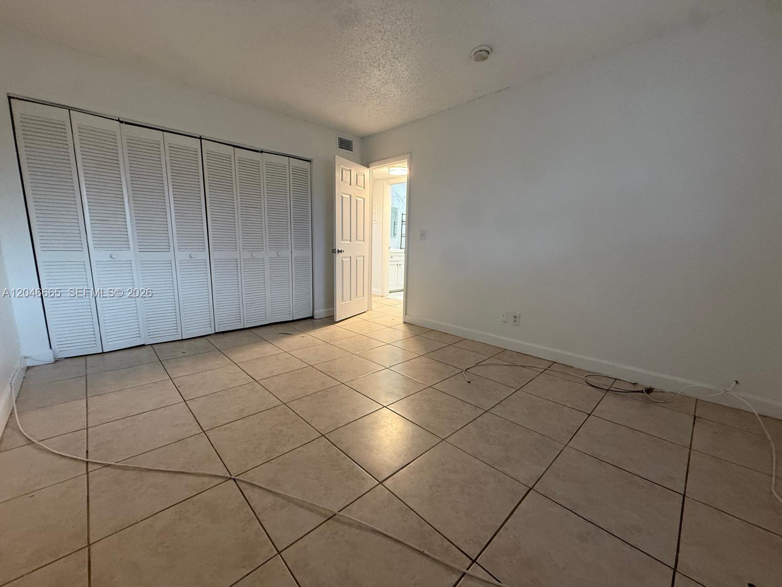 An empty room features beige tile flooring, white walls, louvered closet doors, and an open doorway — 400 NW 65th Ave # 202, Margate FL 33063, MARGATE, FL