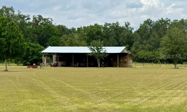 A large, open-sided wooden barn with a metal roof sits in a grassy field — 26645 COUNTY ROAD 33, GROVELAND, FL
