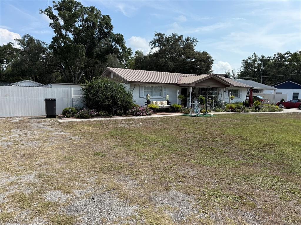 A single-story house with a metal roof, white brick exterior, and a large front yard — 5408 EUREKA SPRINGS ROAD, TAMPA, FL