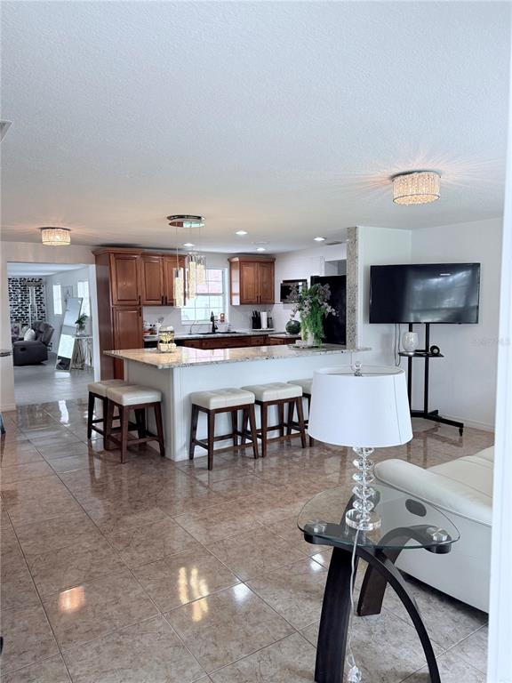 An open-concept kitchen with wood cabinets and a granite island overlooks a tiled living area — 5408 EUREKA SPRINGS ROAD, TAMPA, FL