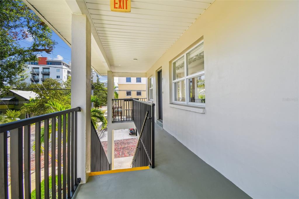 An outdoor walkway with a metal railing leads to a building entrance and stairs — 210 6TH AVENUE N UNIT 9, ST PETERSBURG, FL