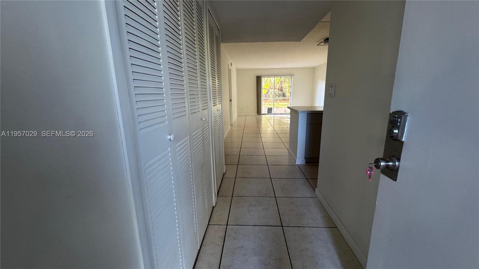 A tiled hallway leads past louvered closet doors toward a kitchen and living area — 4111 Stirling Rd # 102, Dania Beach FL 33314, DANIA BEACH, FL