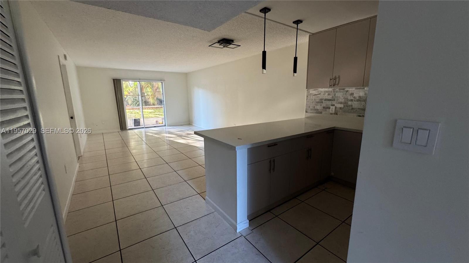 A kitchen with a breakfast bar and tile flooring opens into a living area — 4111 Stirling Rd # 102, Dania Beach FL 33314, DANIA BEACH, FL