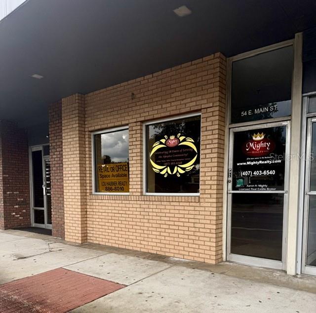 A brick commercial building exterior features two large windows and a glass entrance door — 54 E MAIN STREET, APOPKA, FL