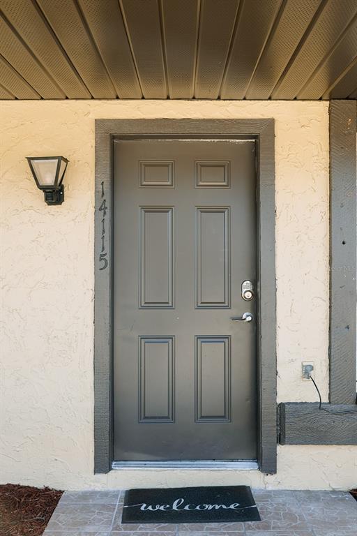 A dark gray six-panel front door with a digital lock and house numbers on the side — 14115 VILLAGE VIEW DRIVE, TAMPA, FL