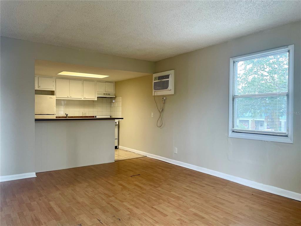 An interior view of a living room with wood-look flooring, a window, and an open kitchen — 5101 CURRY FORD ROAD UNIT 4, ORLANDO, FL