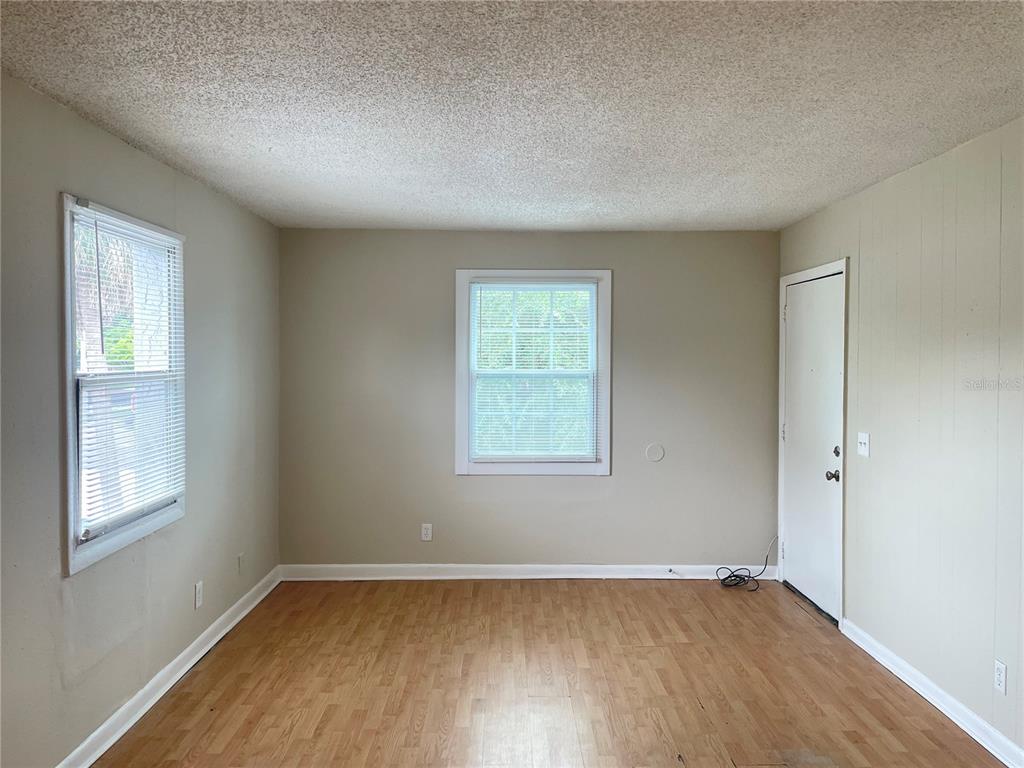 An empty room features light-colored walls, wood-look flooring, two windows with blinds, and a door — 5101 CURRY FORD ROAD UNIT 4, ORLANDO, FL