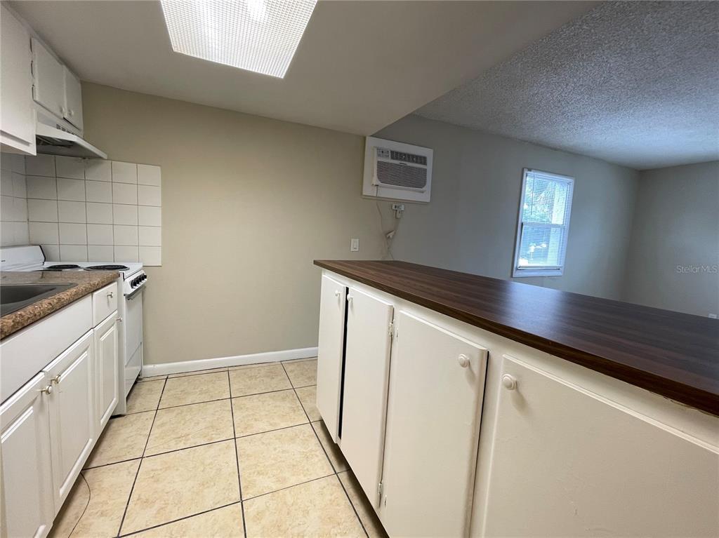 A kitchen features white cabinets, a dark wood countertop, tiled flooring, and a wall-mounted air conditioner — 5101 CURRY FORD ROAD UNIT 4, ORLANDO, FL
