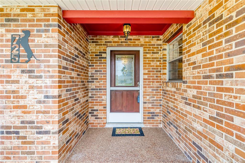 A brick-walled entryway features a brown front door with a glass insert and a doormat — 725 GREEN ROAD, NEW SMYRNA BEACH, FL