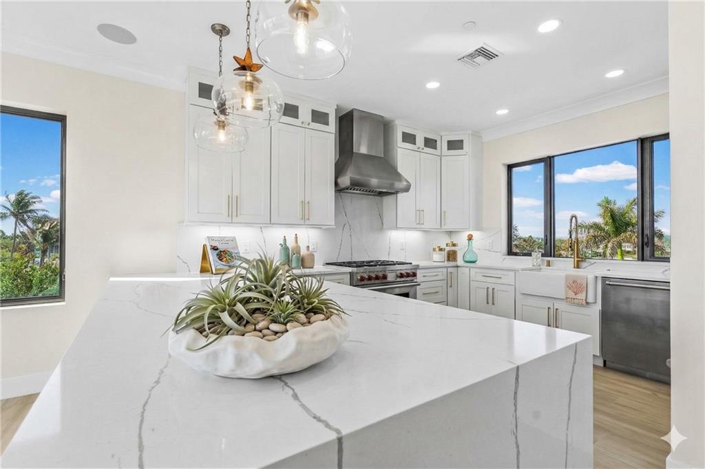 A modern kitchen features white marble countertops, white cabinetry, stainless steel appliances, and large windows — HUTCHINSON ISLAND, FL