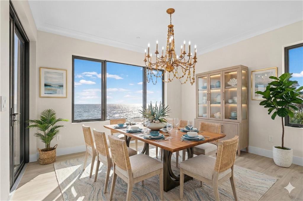 A dining room with a wooden table, chandelier, and large windows overlooking the ocean — HUTCHINSON ISLAND, FL