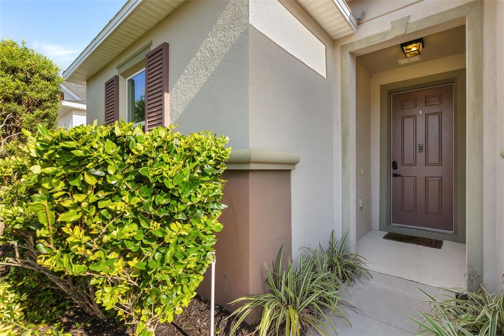 A brown front door is recessed into a beige stucco home with a manicured bush — 12025 SUMTER DRIVE, ORLANDO, FL