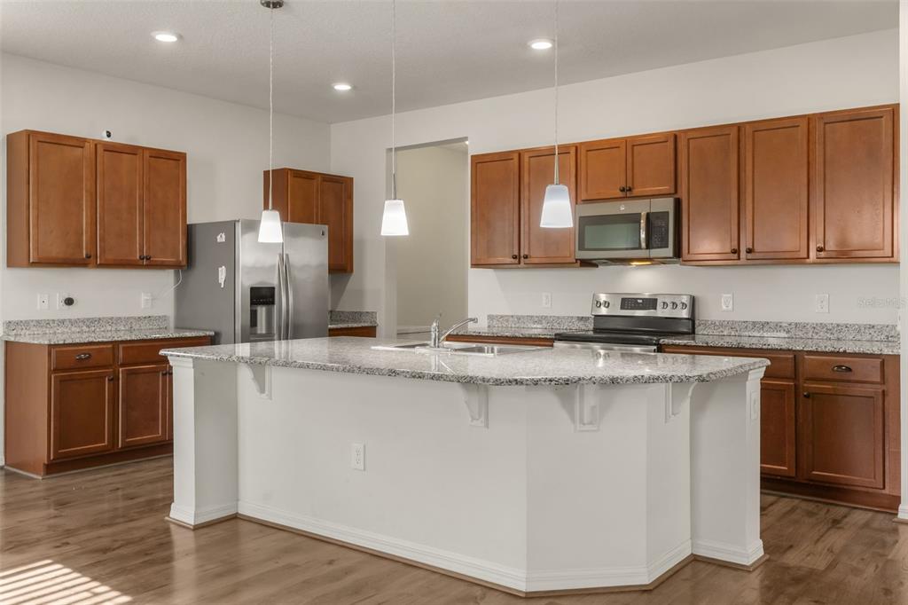 A kitchen with wood cabinets, granite countertops, a central island, and stainless steel appliances — 12025 SUMTER DRIVE, ORLANDO, FL