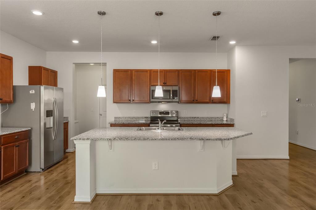 A kitchen features wood cabinets, granite countertops, a center island, and stainless steel appliances — 12025 SUMTER DRIVE, ORLANDO, FL