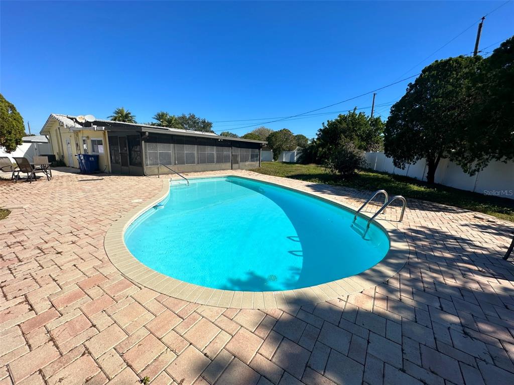 A kidney-shaped swimming pool sits on a brick paver patio next to a screened enclosure — 1770 63RD AVENUE N, ST PETERSBURG, FL