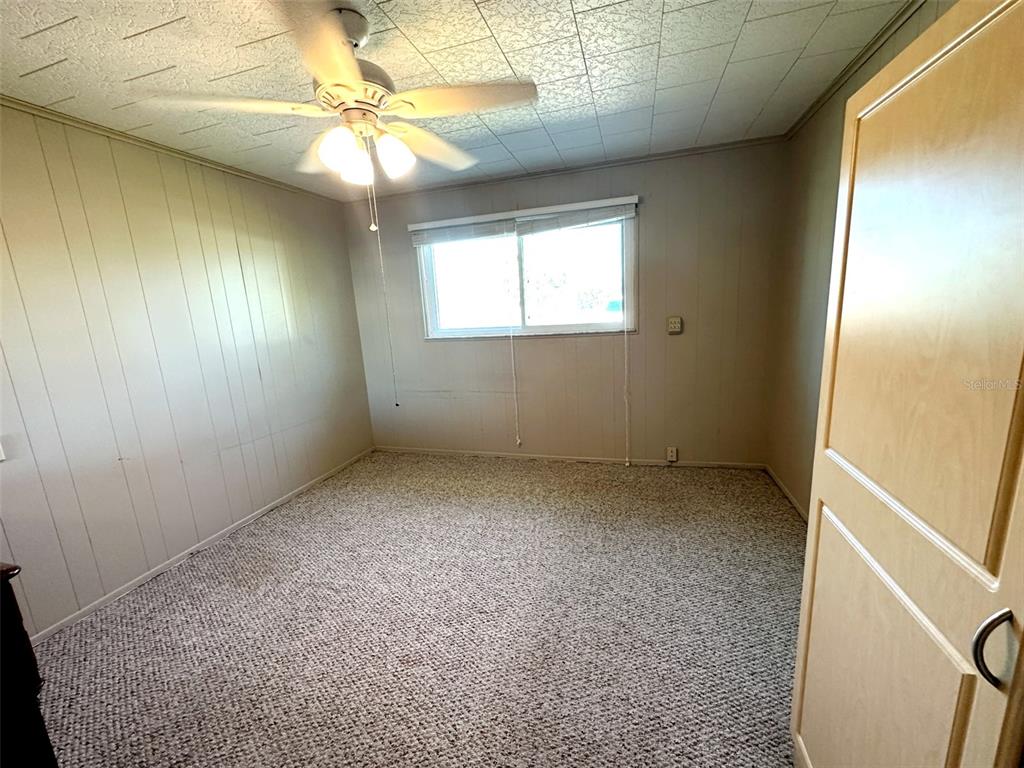 An empty bedroom features wood-paneled walls, a ceiling fan, a window, and carpeted flooring — 1770 63RD AVENUE N, ST PETERSBURG, FL