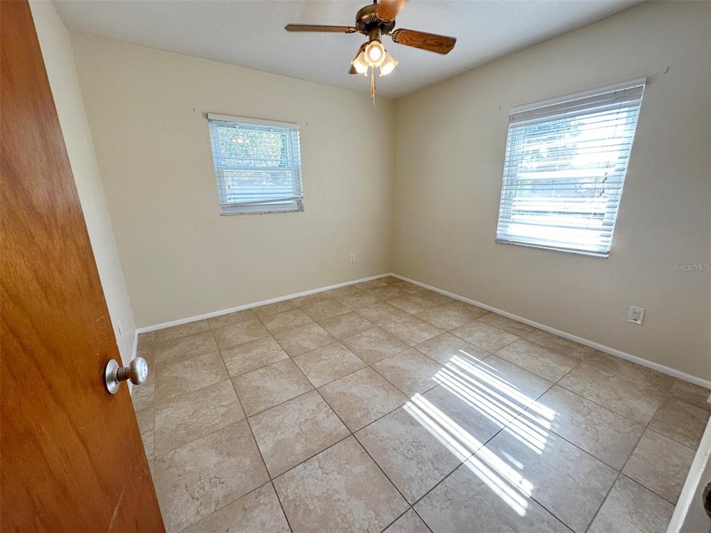 An empty bedroom features beige walls, tile flooring, a ceiling fan, and two windows — 1770 63RD AVENUE N, ST PETERSBURG, FL