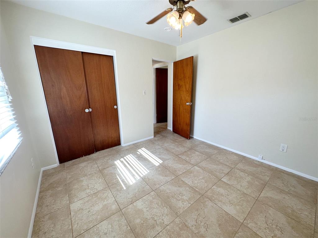 A bedroom with beige walls, tile flooring, a ceiling fan, and wooden doors — 1770 63RD AVENUE N, ST PETERSBURG, FL