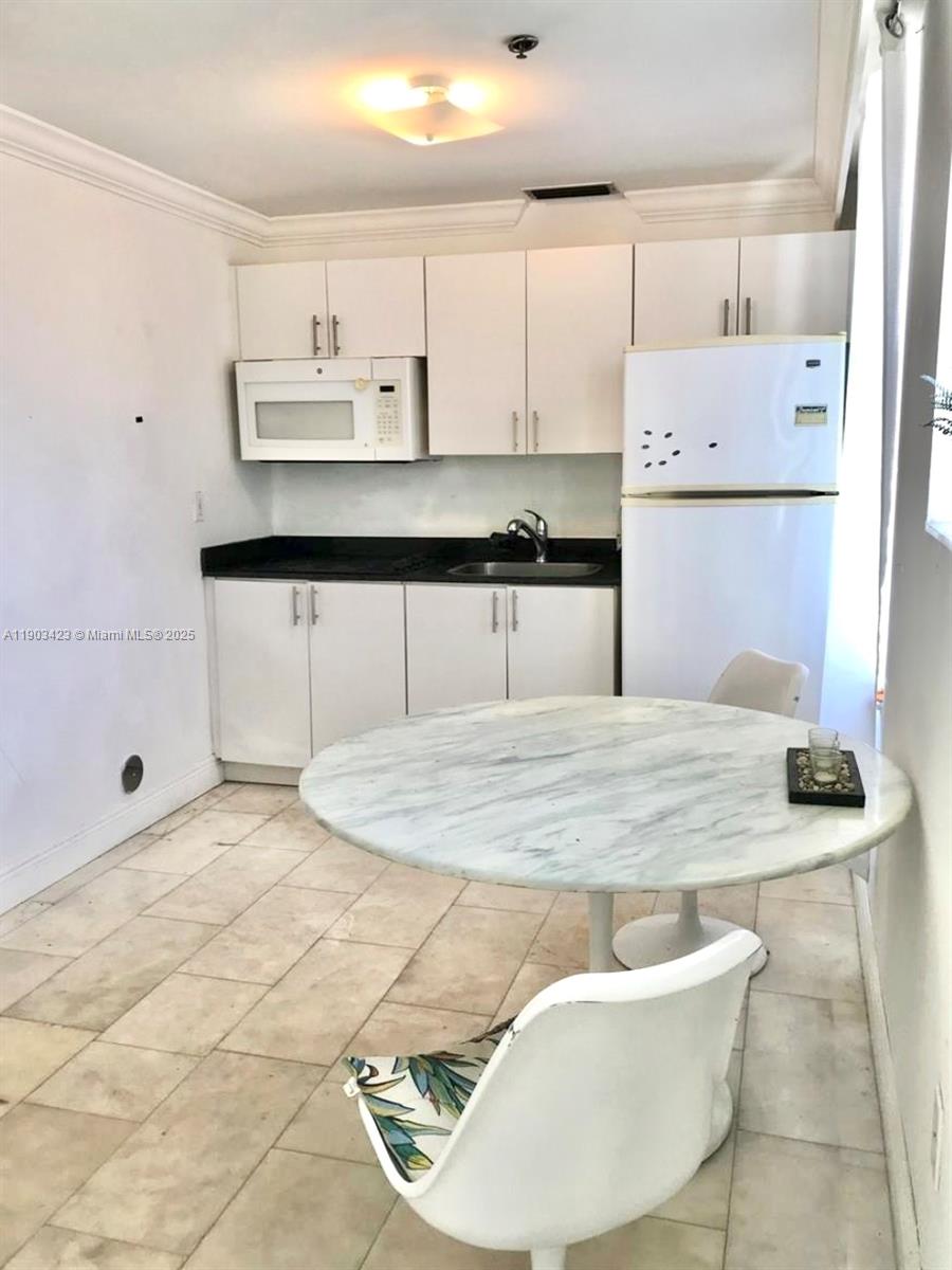 A small kitchen features white cabinets, a white refrigerator, and a round marble dining table — 1502 Jefferson Ave # 104, Miami Beach FL 33139, MIAMI BEACH, FL