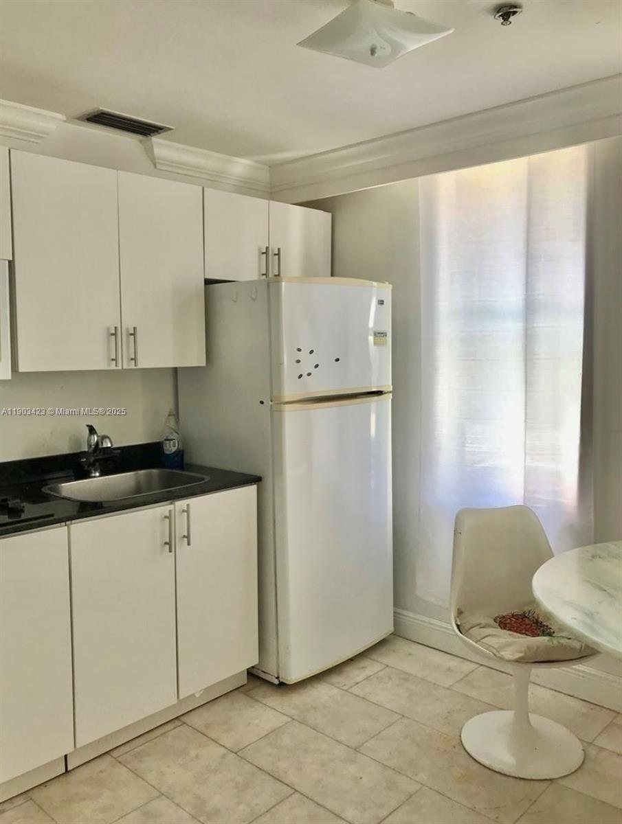 A kitchen features white cabinets, a black countertop, a stainless steel sink, and a refrigerator — 1502 Jefferson Ave # 104, Miami Beach FL 33139, MIAMI BEACH, FL