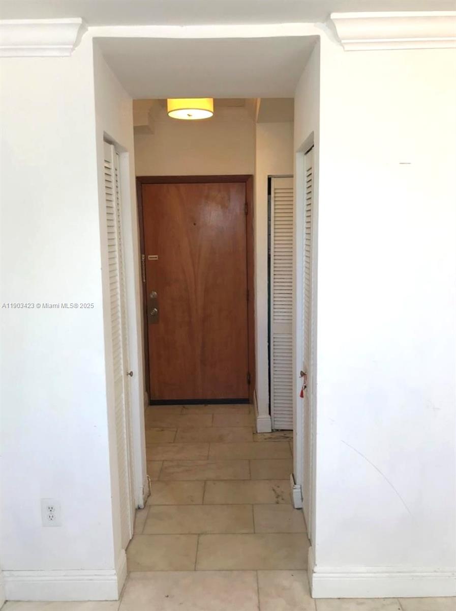 A hallway features a wooden front door, tiled flooring, and white louvered closet doors — 1502 Jefferson Ave # 104, Miami Beach FL 33139, MIAMI BEACH, FL