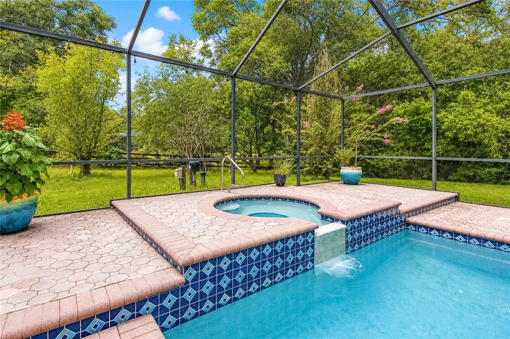 A screened-in pool and spa area with brick pavers and a blue tiled spillover feature — 20130 SW 95TH STREET, DUNNELLON, FL