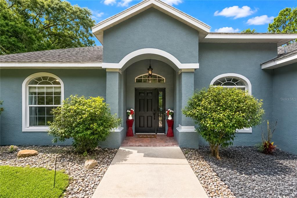 A blue house exterior features a covered entryway, a dark front door, and two bushes — 20130 SW 95TH STREET, DUNNELLON, FL
