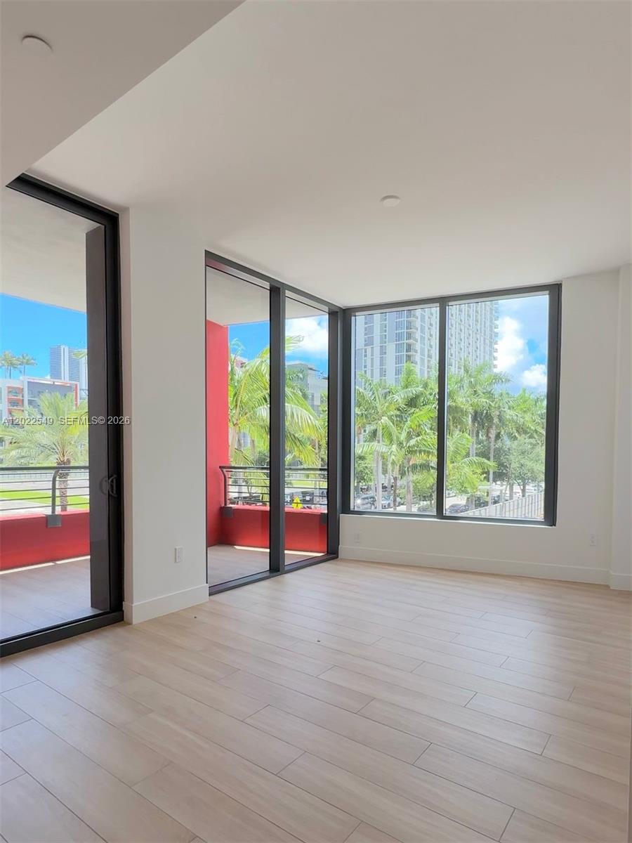 An empty room with light wood floors, floor-to-ceiling windows, and access to a red balcony — 90 NE 32nd ST # 201, Miami FL 33145, MIAMI, FL