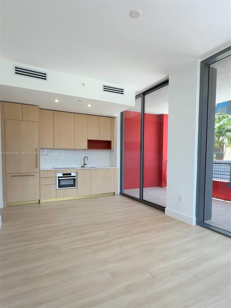 A modern kitchen with light wood cabinetry and stainless steel appliances opens to a balcony — 90 NE 32nd ST # 201, Miami FL 33145, MIAMI, FL