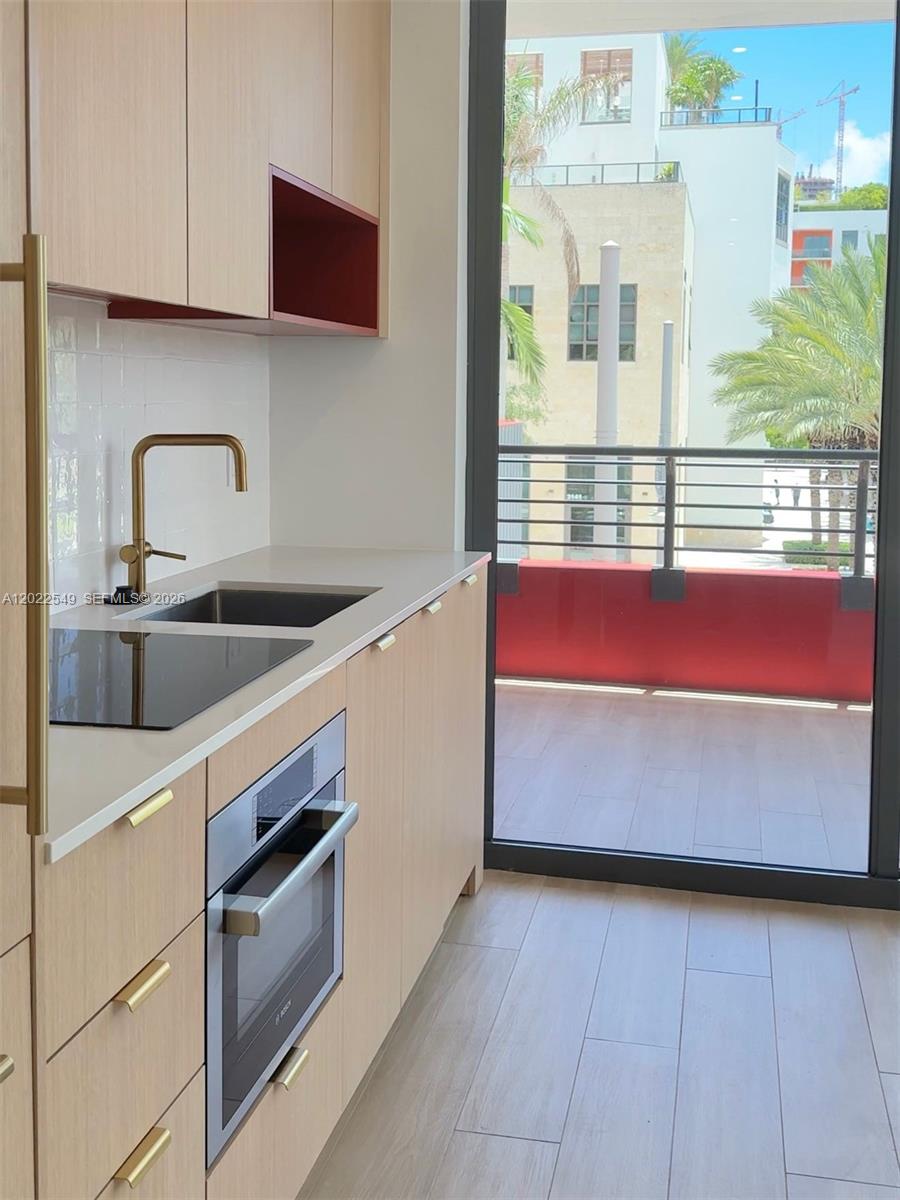 A modern kitchen features light wood cabinetry, gold hardware, and a balcony with outdoor views — 90 NE 32nd ST # 201, Miami FL 33145, MIAMI, FL