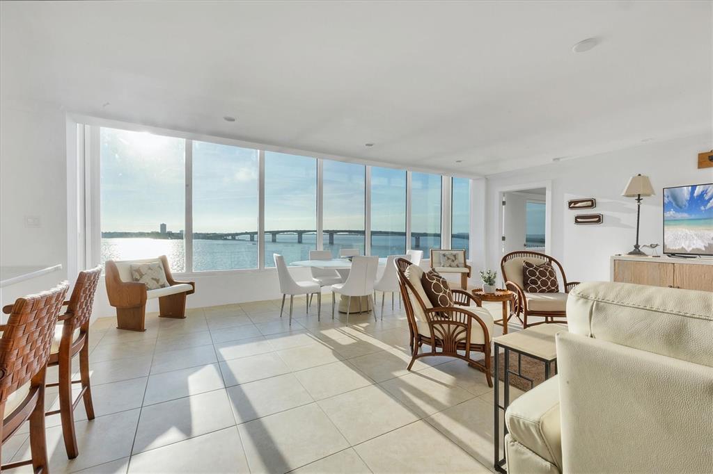A bright living and dining area features floor-to-ceiling windows overlooking a bridge and water — 350 GOLDEN GATE POINT UNIT 62, SARASOTA, FL