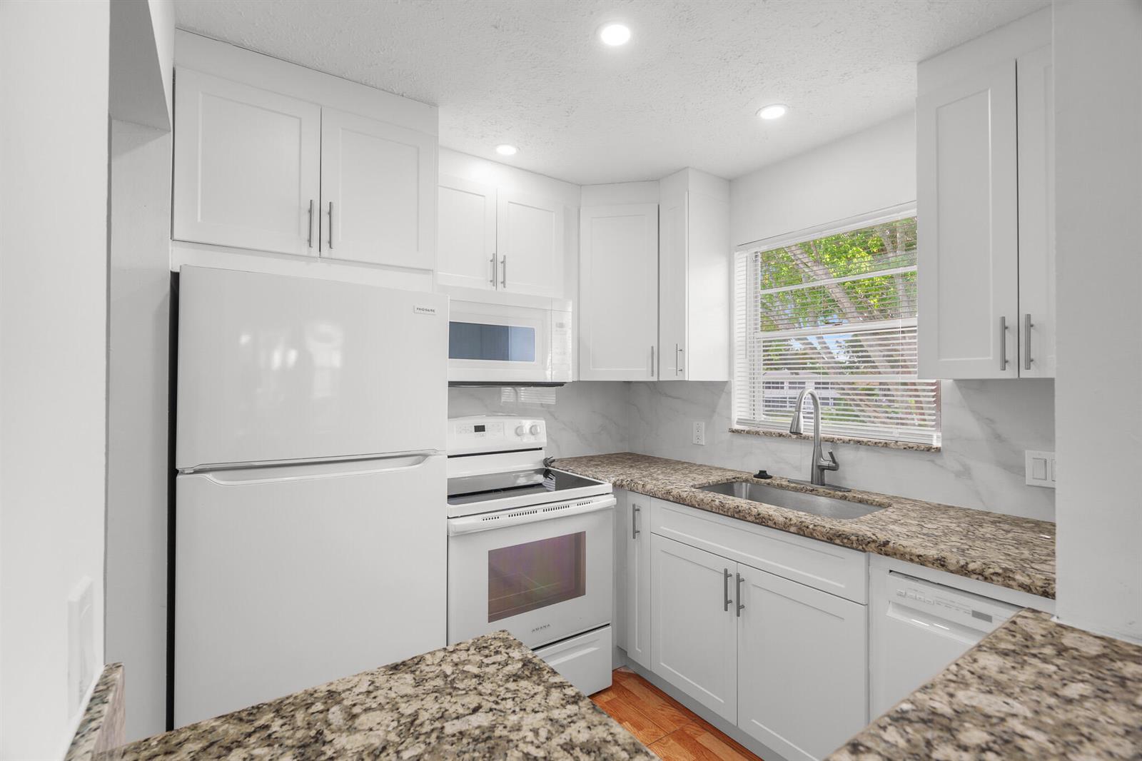 A kitchen features white cabinets, granite countertops, white appliances, and a window above the sink — 346 Windsor O, West Palm Beach FL 33417, WEST PALM BEACH, FL