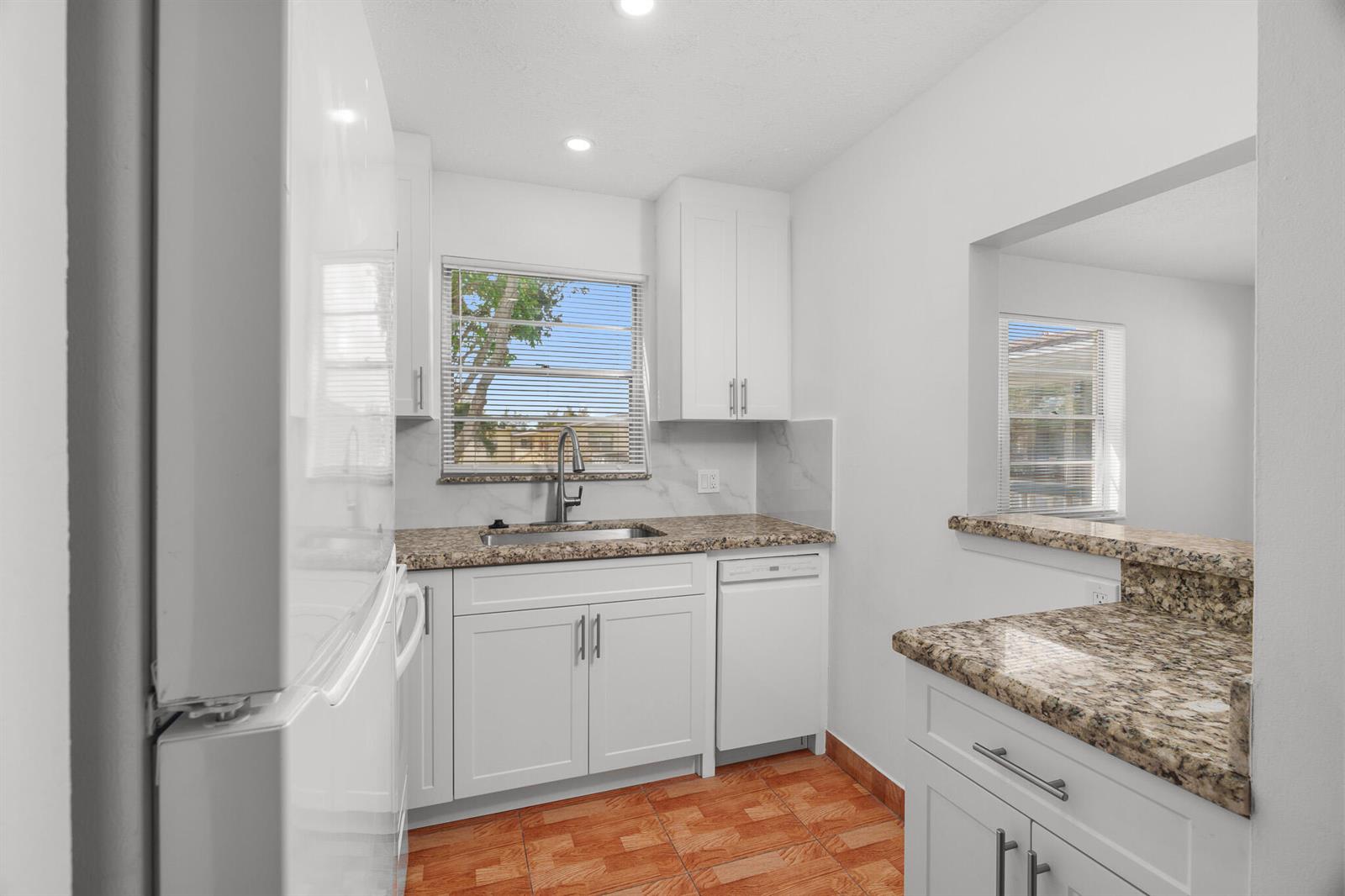 A kitchen features white cabinets, granite countertops, a white refrigerator, and orange tiled flooring — 346 Windsor O, West Palm Beach FL 33417, WEST PALM BEACH, FL