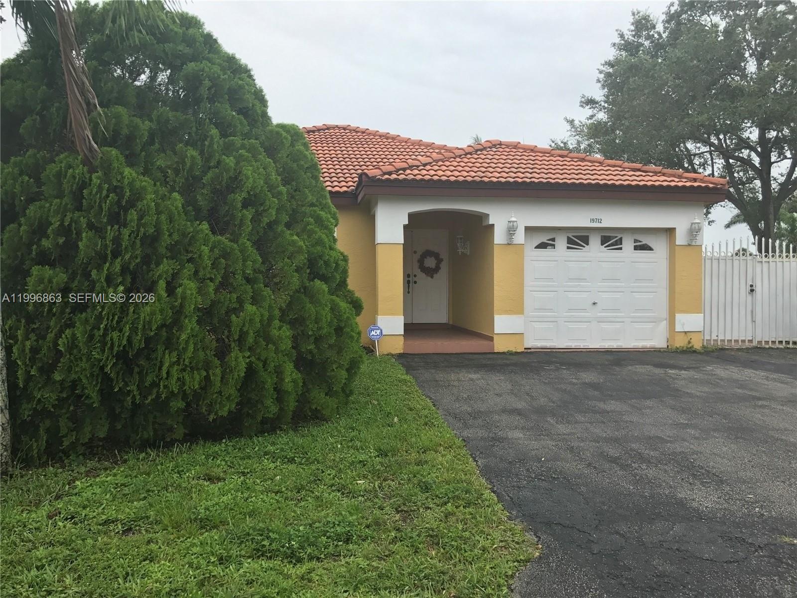 A yellow single-story house features a red tile roof, a white garage, and landscaping — 19712 NW 82nd Pl, Hialeah FL 33015, HIALEAH, FL